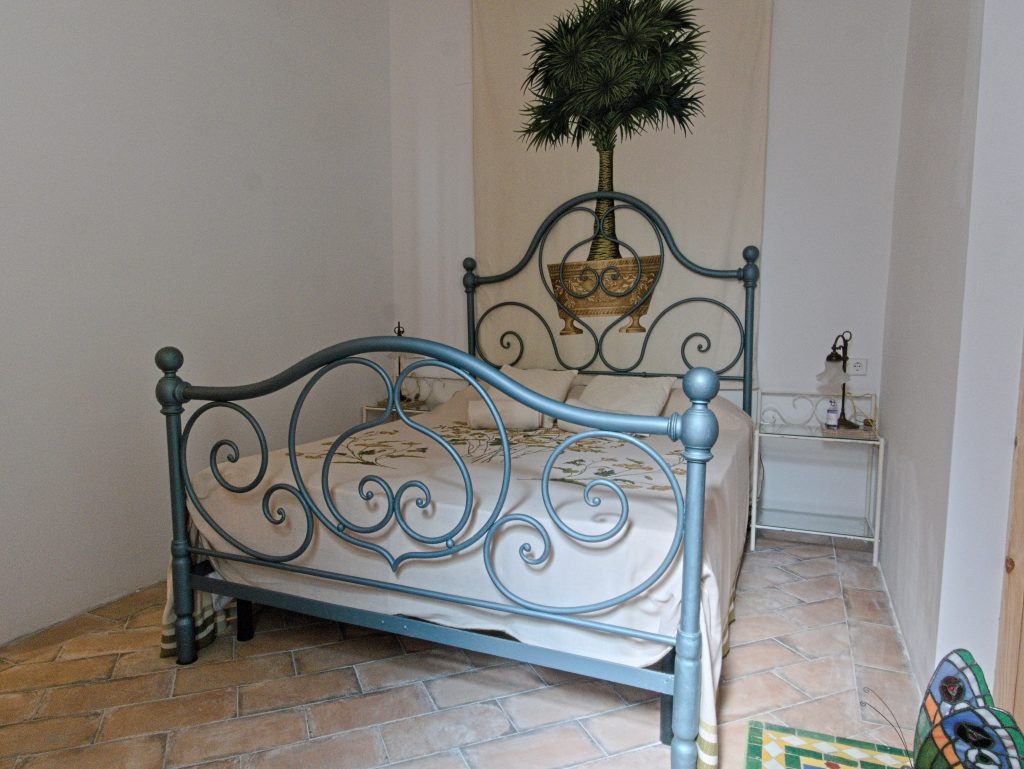 Bedroom with blue wrought-iron bed and palm tree tapestry at Casa Mayolica apartment, Manises