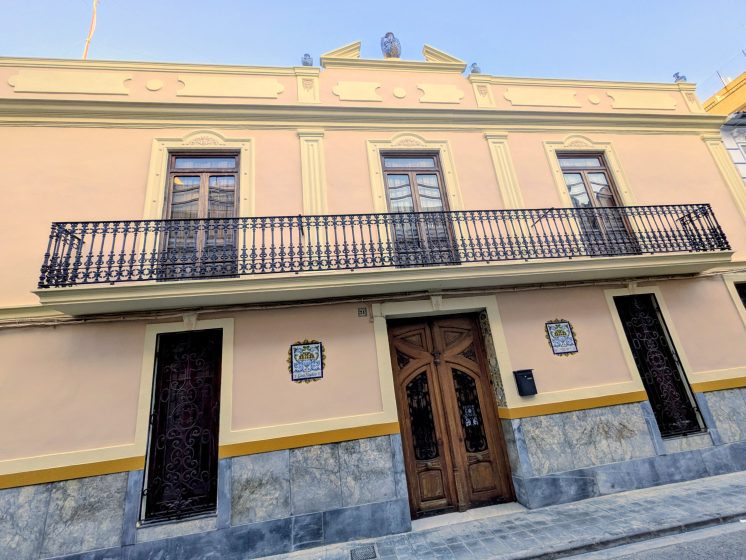The facade of Casa Mayolica in Manises on a sunny day, with ceramic vases along the roofline and a wrought-iron balcony